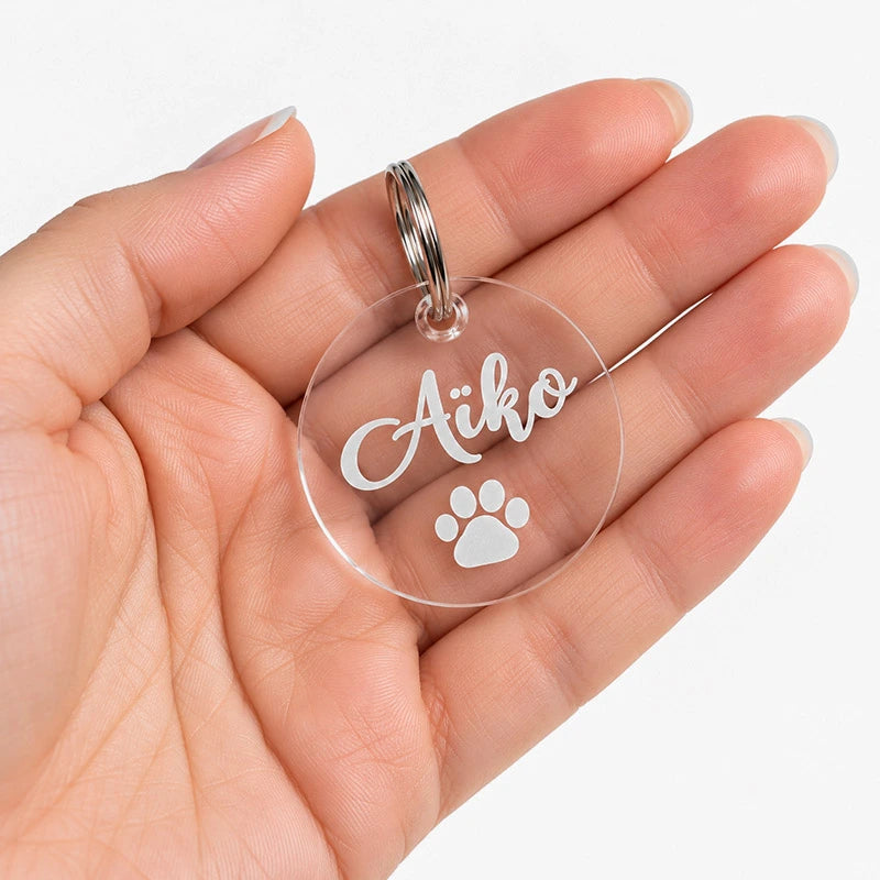 Grande médaille transparente de 40 mm pour chien ou chat, gravée au prénom « Aïko » avec une patte, tenue dans la main