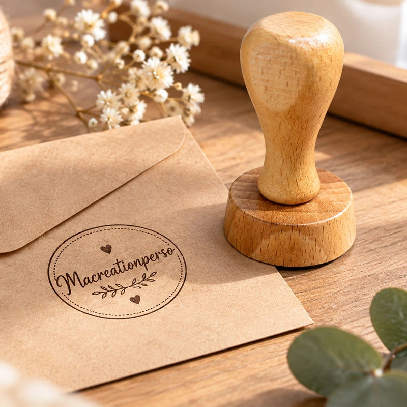 Tampon en bois personnalisé avec logo, posé sur une enveloppe kraft tamponnée, au milieu de fleurs séchées